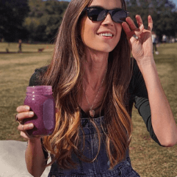 Woman in sunglasses holding a purple sea moss mason jar outdoors